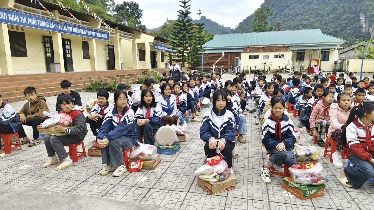 Các em học sinh ngồi trên sân trường cùng những phần quà